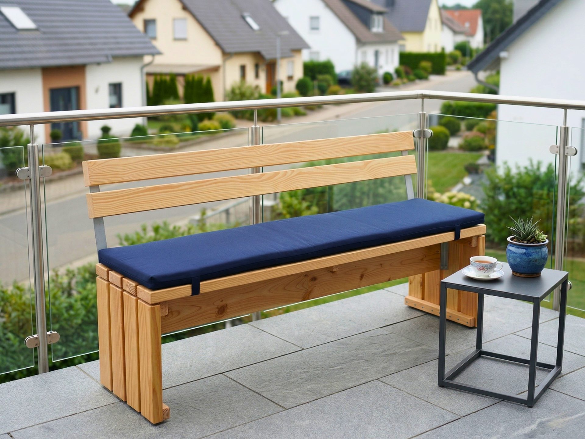 Gartenbank mit Rückenlehne aus Douglasie und blauem Polster auf Balkon als bequemes Sitzmöbel.