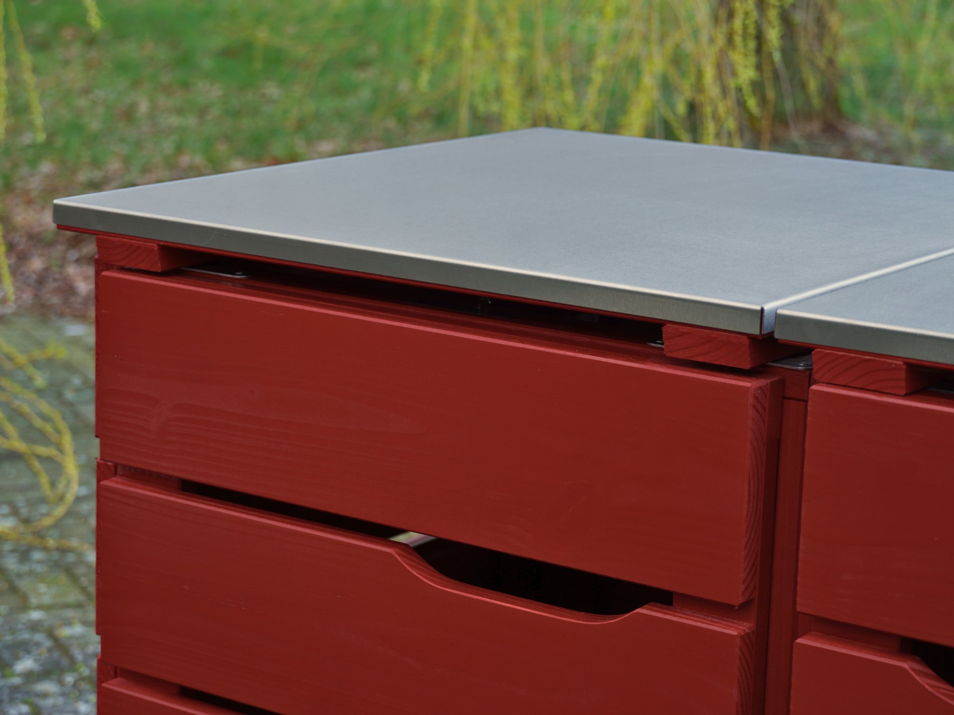 Detailaufnahme des linken Deckels und Tür-Ausschnitts der Mülltonnenbox in Nordisch Rot mit Edelstahl-Deckel