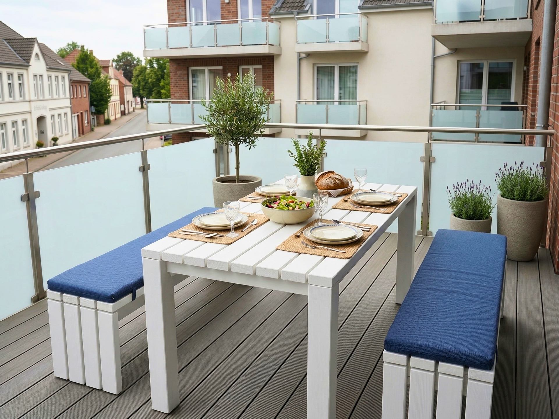 Gartenmöbel Set in Weiß mit Tisch und zwei Bänken für bis zu 6 Personen auf einem Balkon.