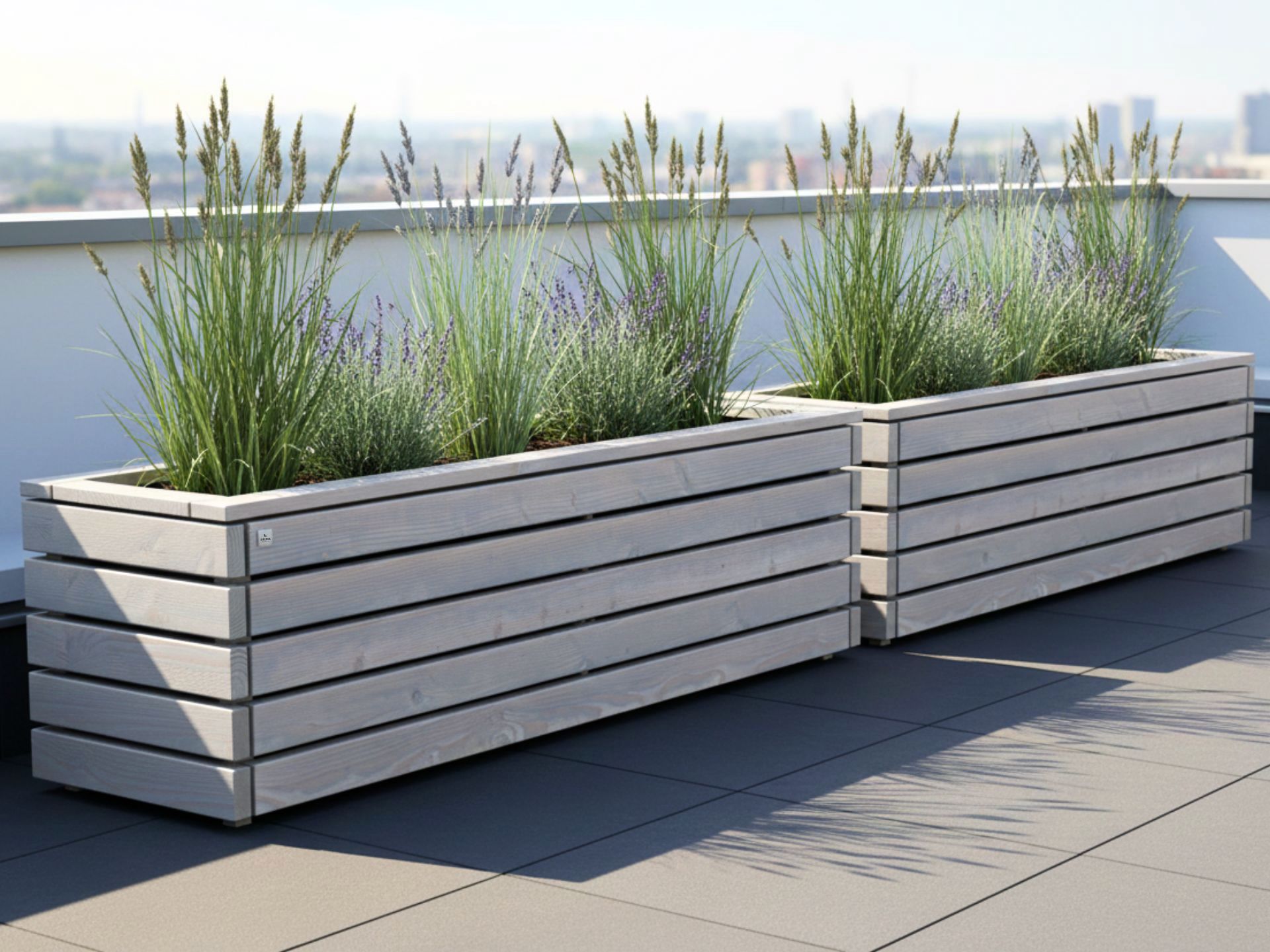 Zwei Pflanzkästen ClassicPlus 200×50×57 cm in Grau Geölt auf einer Dachterrasse, bepflanzt mit hohen Gräsern.