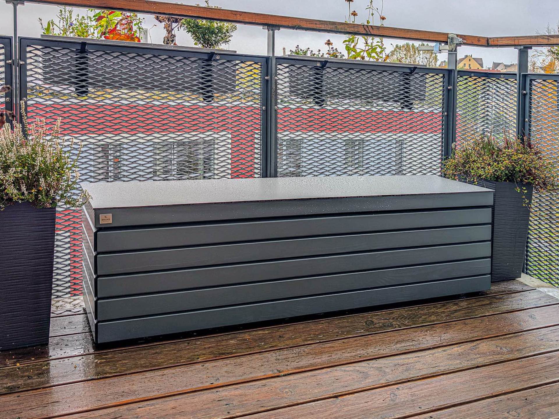 Moderne Gartenbox in Rhombus-Optik mit Deckel aus Design-Outdoor-Platte auf Balkon mit Holzdielen und Metall-Geländer