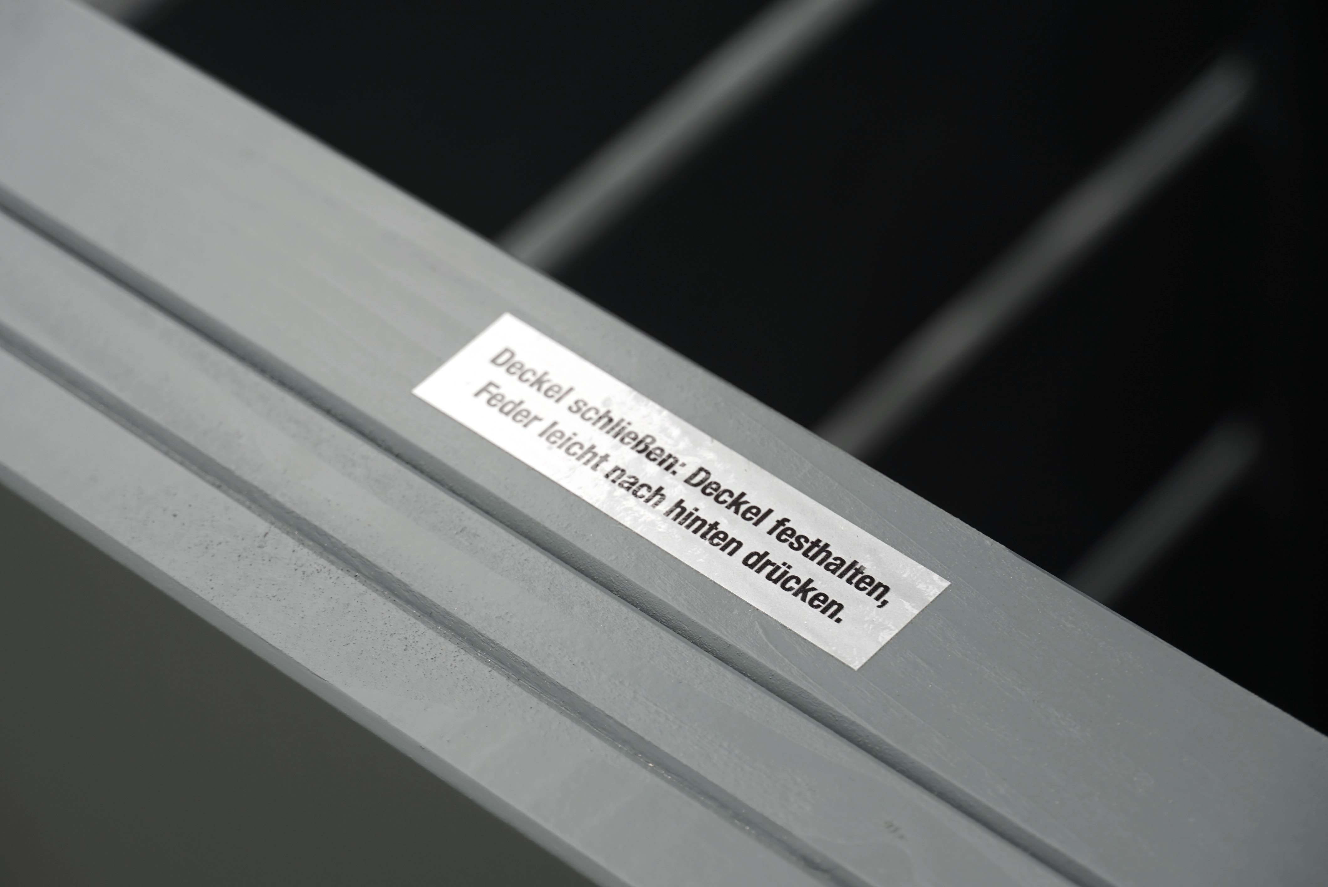 Geöffnete Mülltonnenbox in Grau, Blick ins Innere mit Bedienungshinweis