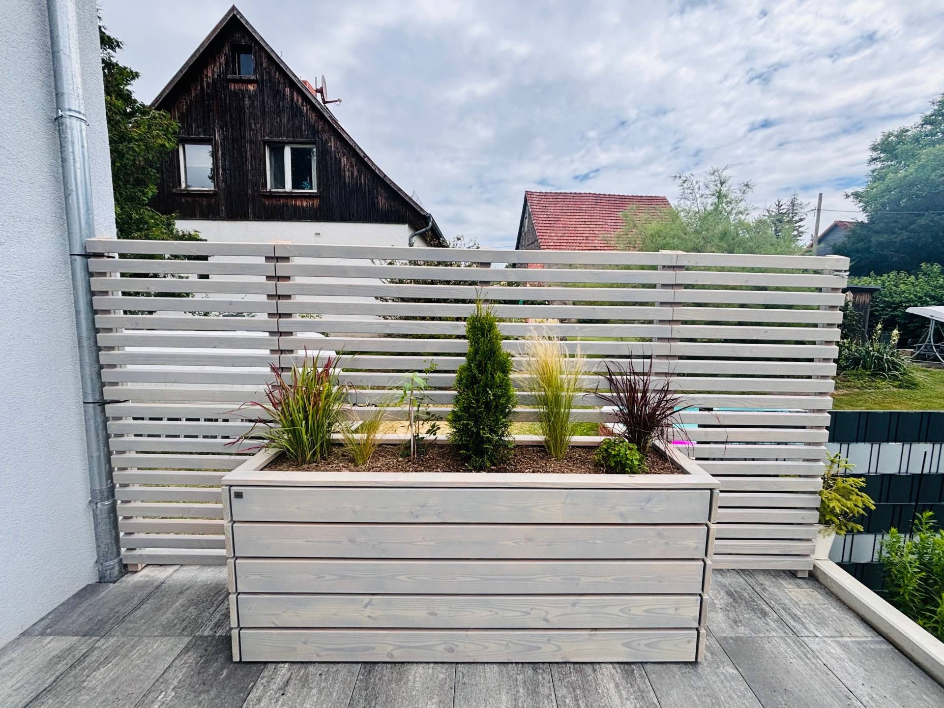 Großer Pflanzkasten mit Sichtschutz in Grau Geölt und hohen Gräsern auf einer als Terrasse genutzten Dachgarage.