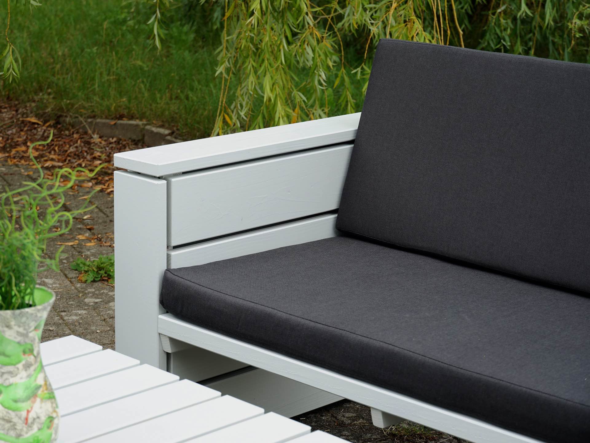 Sofa in lichtgrau lackierter Douglasie, Sitz- und Rückenpolster in Anthrazit, linke Armlehne im Vordergrund