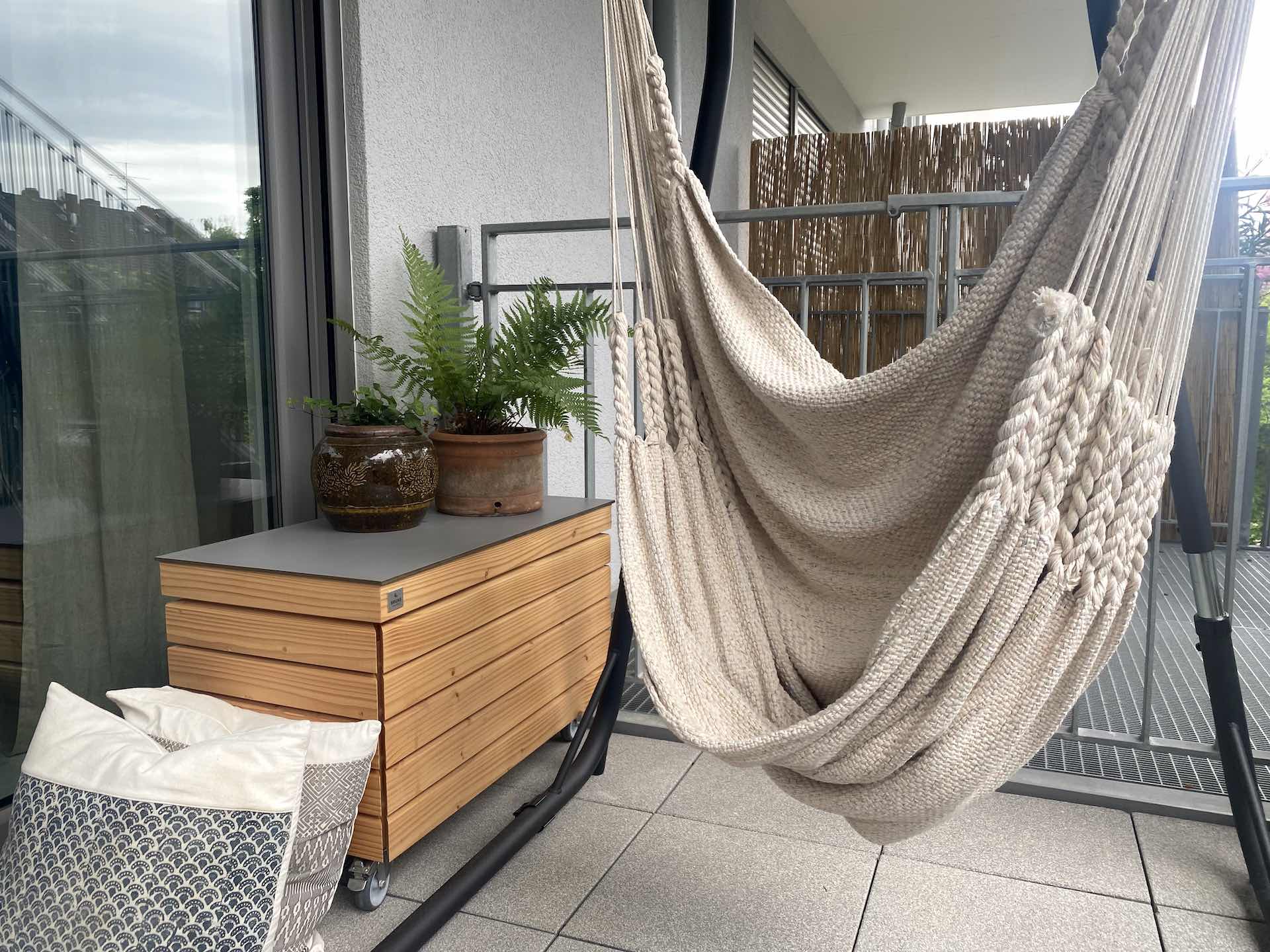 Gartenbox auf Rollen mit wetterfestem Deckel auf Balkon Gesamtansicht einer mobilen Gartenbox mit grauer Deckelverkleidung auf Balkon mit Steinplatten und Metallgeländer