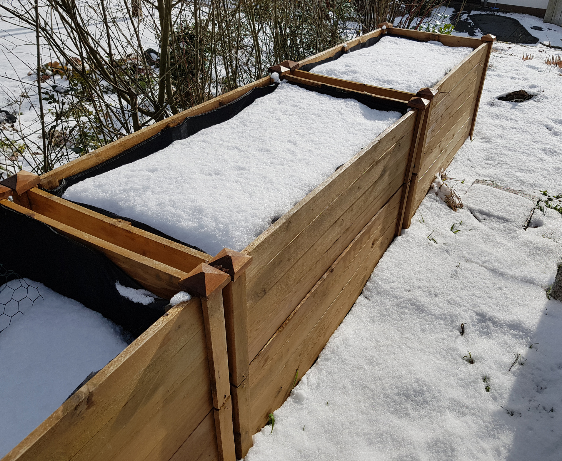 Holz-Hochbeet mit Schnee bedeckt im winterlichen Garten.