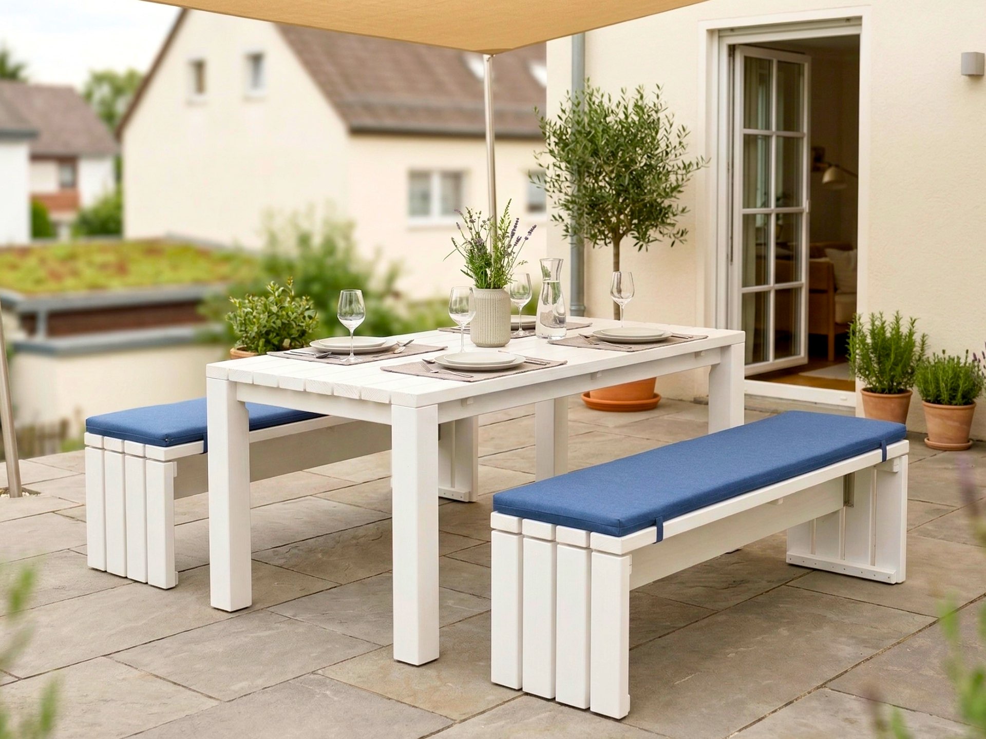 Weiße Essgruppe aus Holz mit Tisch und zwei Bänken für bis zu 6 Personen auf einer Terrasse.