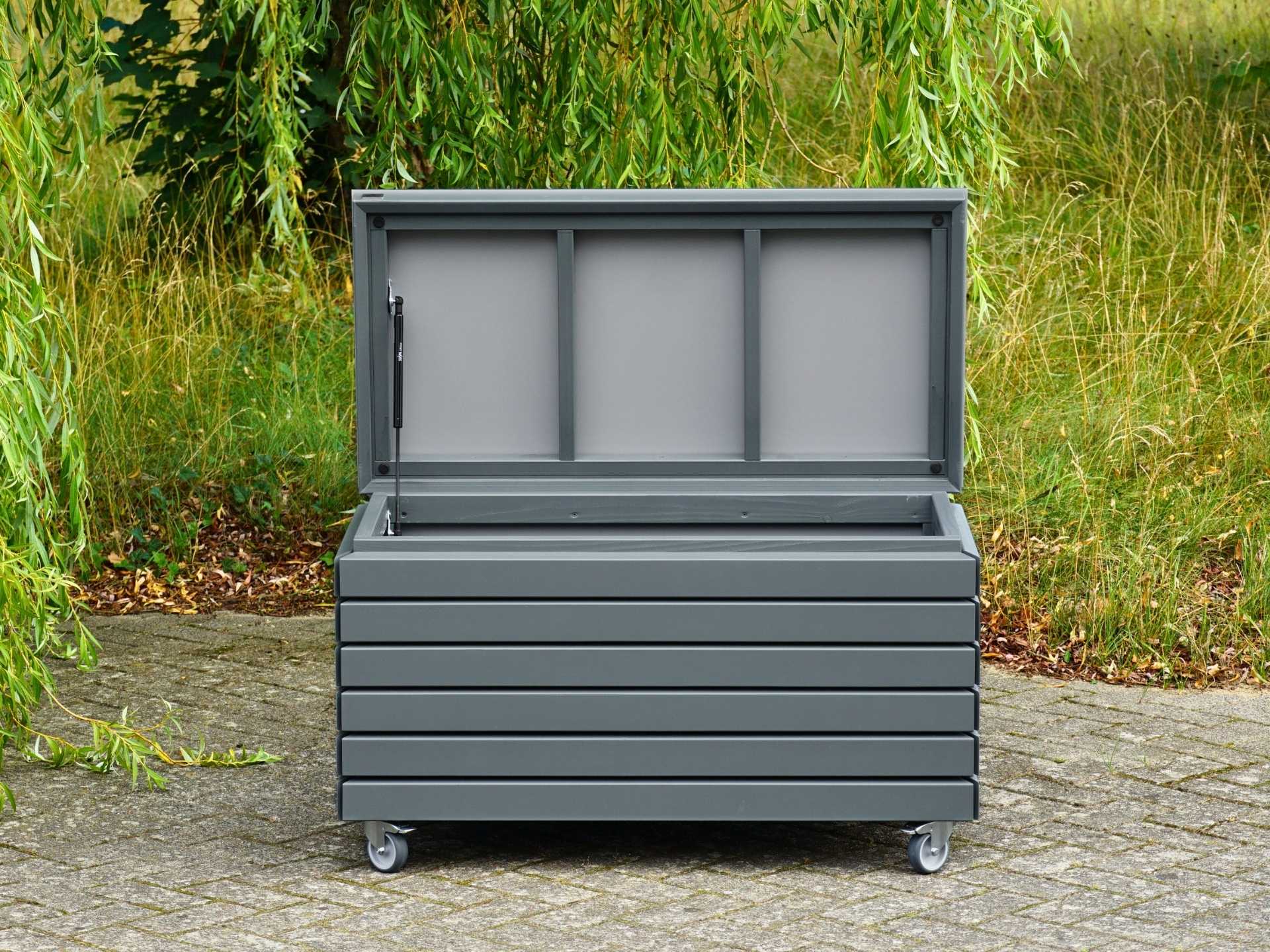 Geöffnete Gartenbox mit Rollen in Basaltgrau, wetterfest aus Holz, mit Gasdruckfeder als Deckelöffner – Auflagenbox, Kissenbox, Sitztruhe.