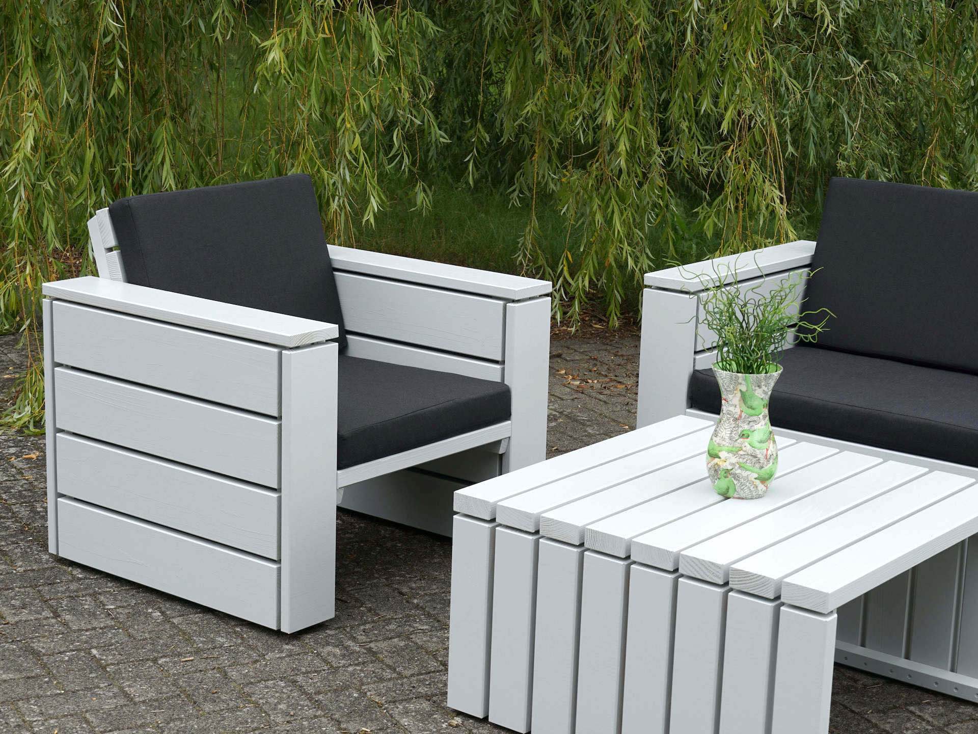 Detailansicht des Loungetischs, lichtgrau lackiert mit sichtbarem Fugenbild, im Hintergrund teilweise Sofa und Sessel mit anthrazitfarbenen Polstern