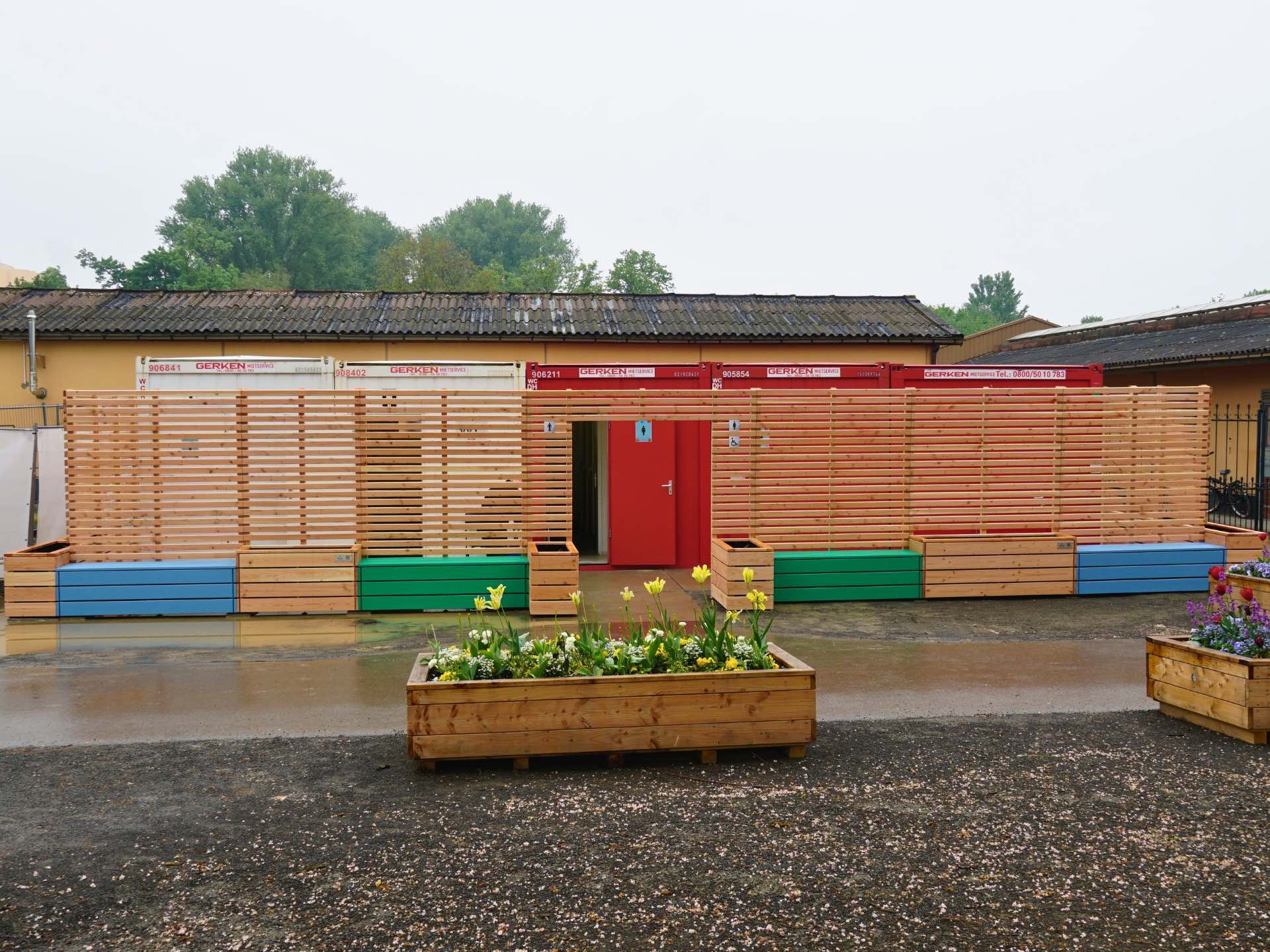 Sichtschutz-Anlage mit abwechselnden Pflanzkästen und Sitzbänken zur Kaschierung von WC-Containern – Frontansicht