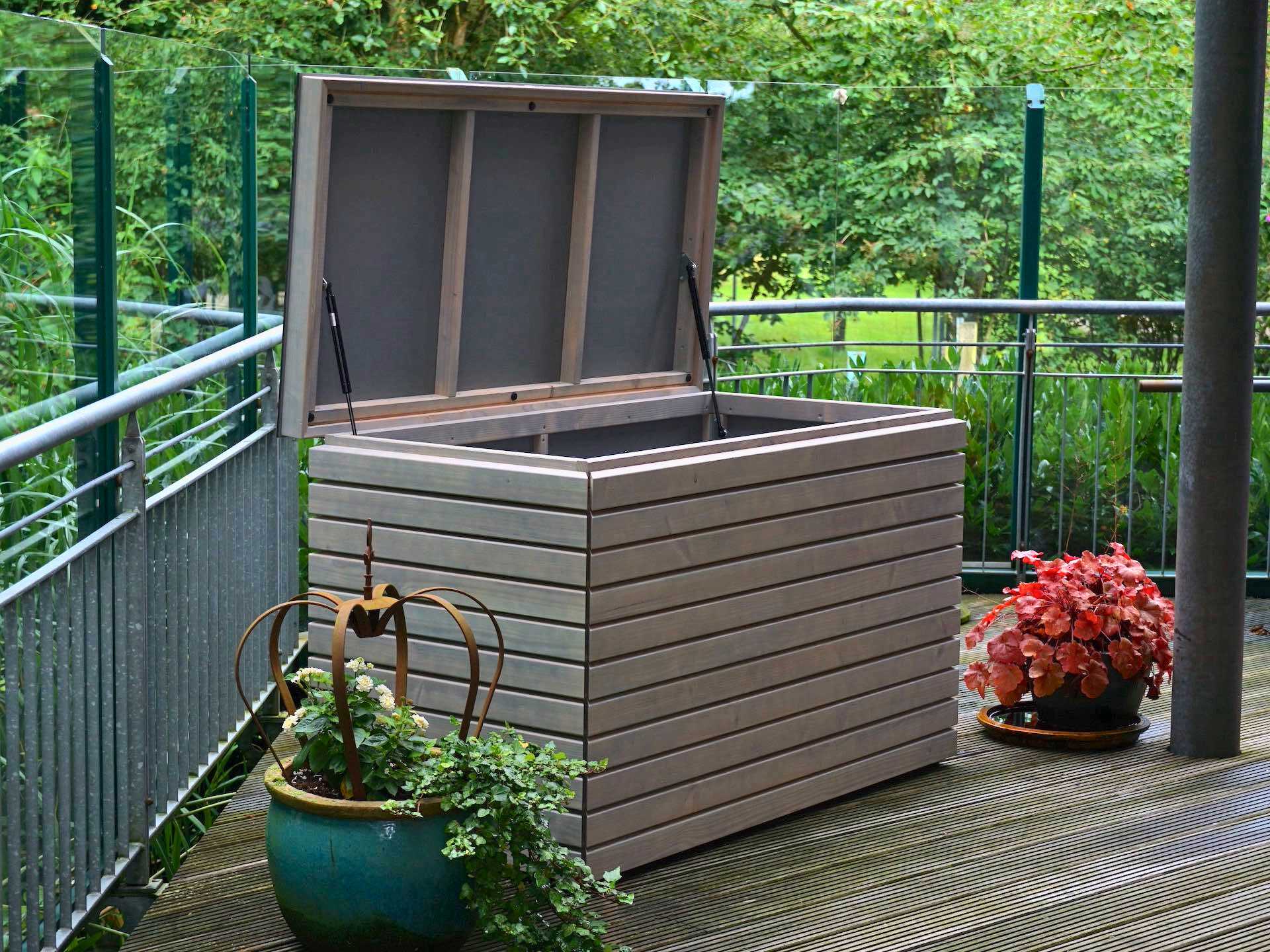 Gartenbox in Grau Geölt – geöffnet von vorn links, Innenraum mit HPL sichtbar, Deckel mit Gasdruckfedern	