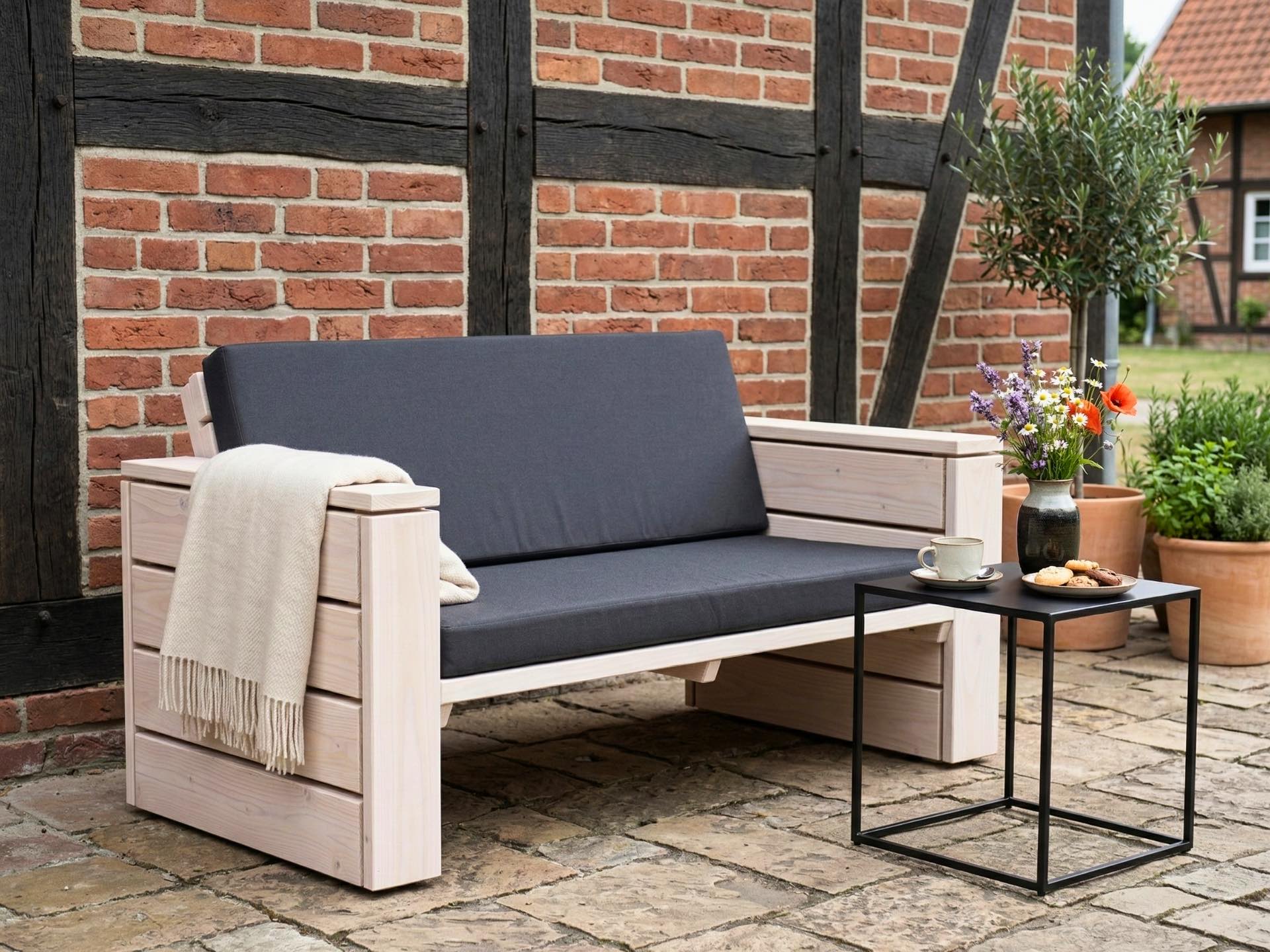 Lounge Sofa 2-Sitzer aus weiß geöltem Holz vor Fachwerkwand als gemütliches Sitzmöbel auf Terrasse.
