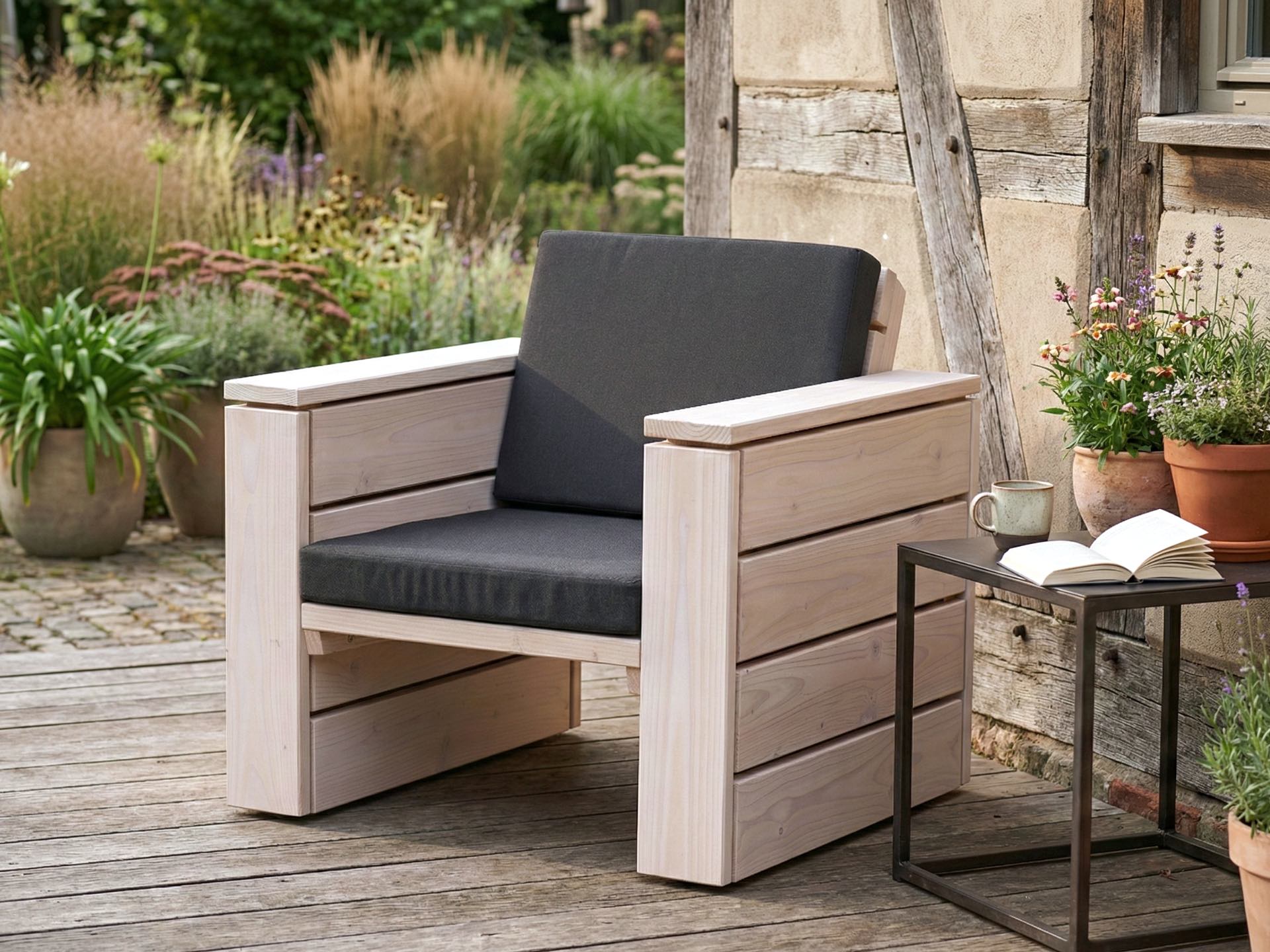 Lounge Sessel aus Holz in Weiß Geölt mit anthrazitfarbenen Polstern vor einer Hauswand.