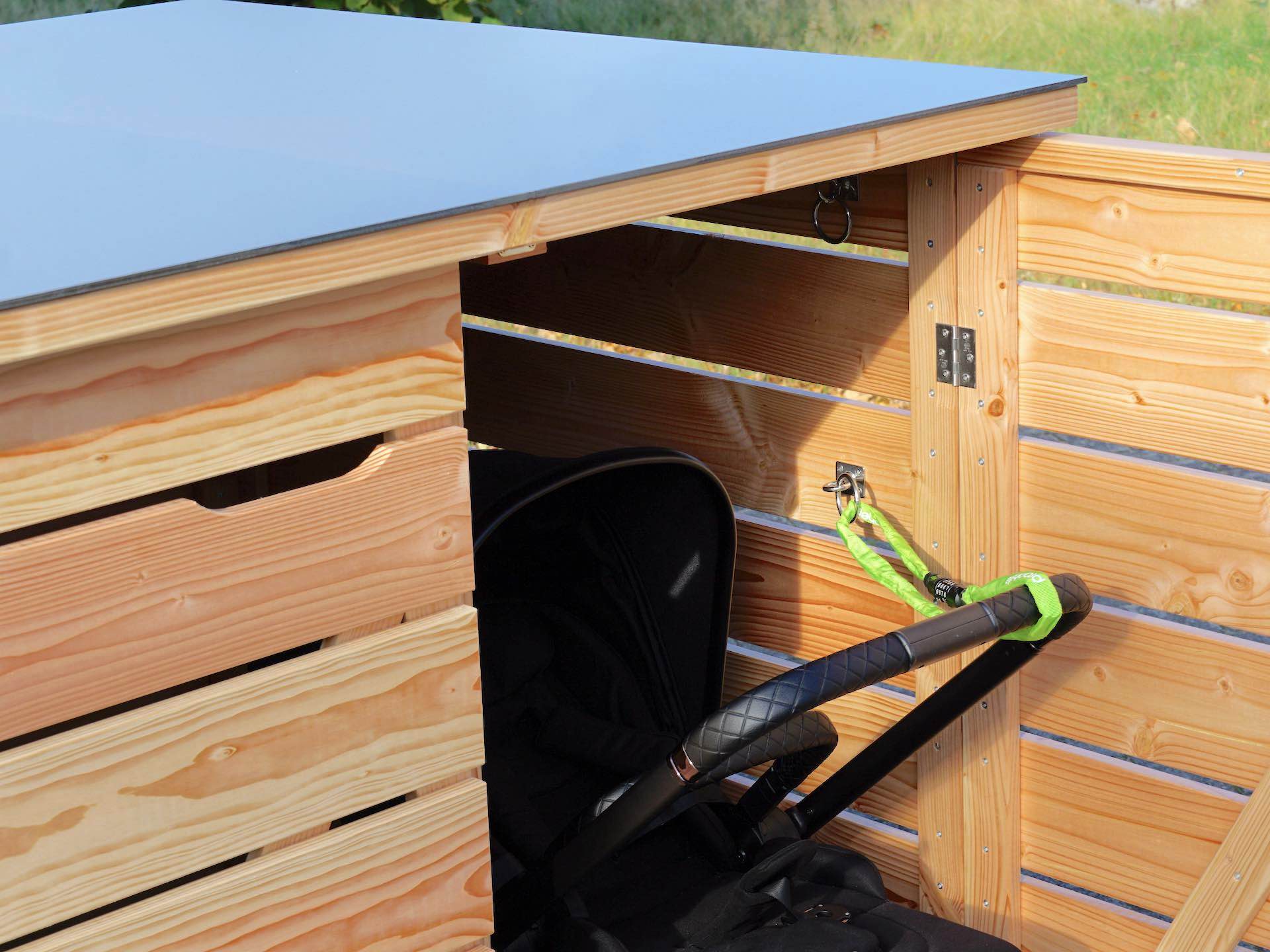 Detailaufnahme durch die geöffnete Tür der Kinderwagenbox – im Innenraum stabile Metallösen zur Sicherung des Kinderwagens