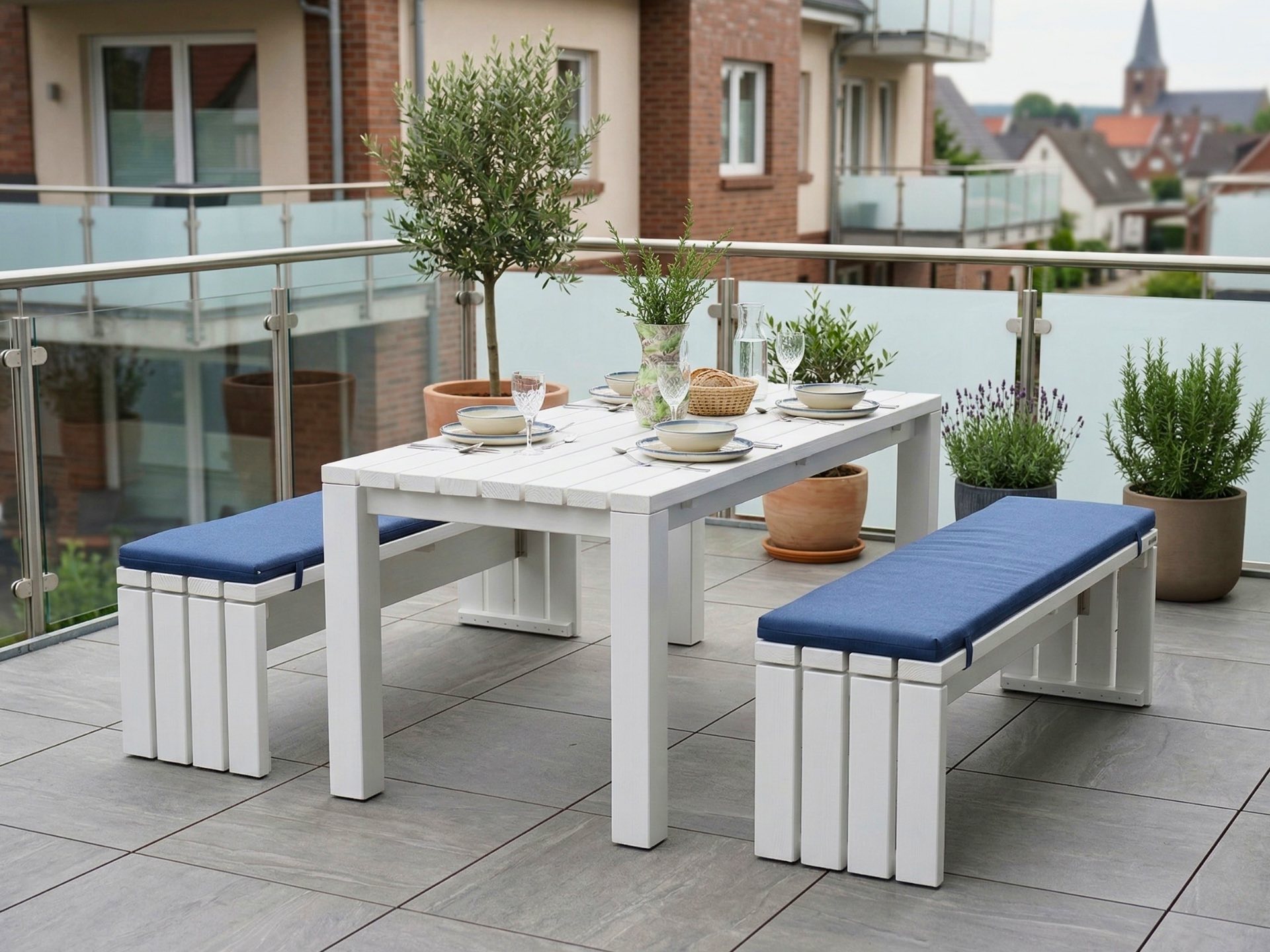 Großes Gartenmöbel Set in Weiß mit Tisch und zwei Bänken mit dunkelblauen Polstern auf einem Balkon.