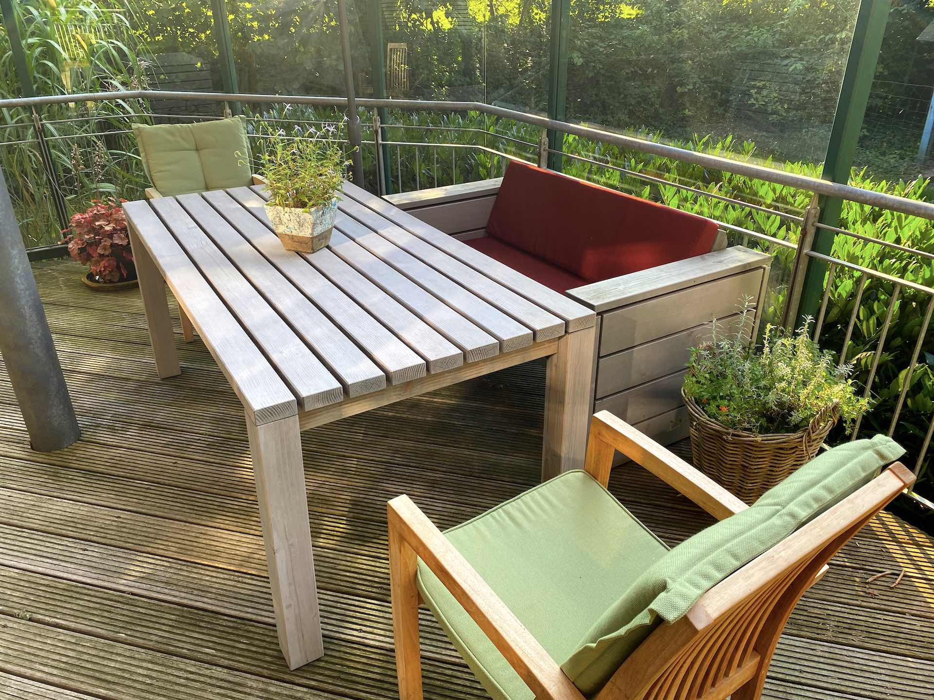 2er Loungesofa grau geölt mit dunkelroten Polstern auf erhöhter Terrasse, hinter passendem Gartentisch