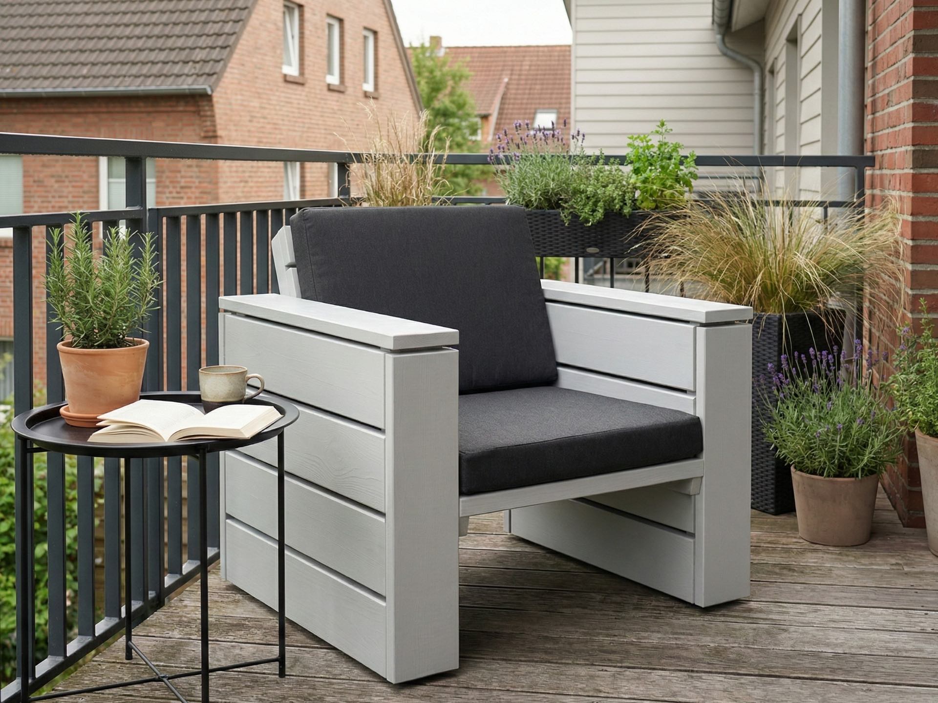 Lounge Sessel aus Holz in Lichtgrau mit anthrazitfarbenen Polstern vor einem modernen Balkon.